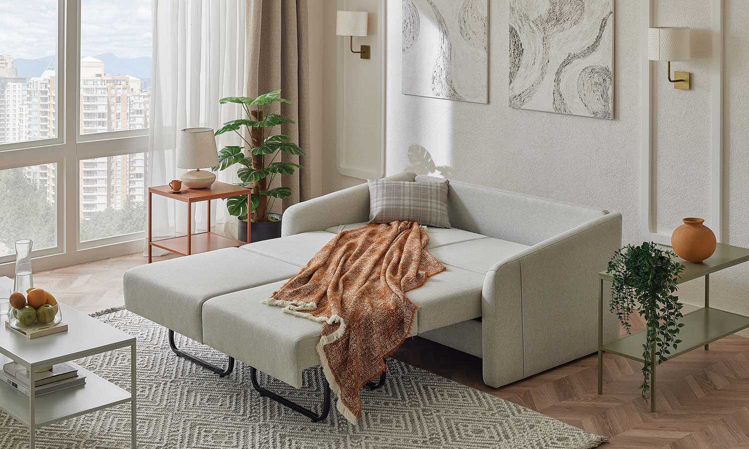 Canapé Ester gris clair déplié en couchage, avec plaid orange et coussin à carreaux